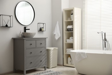 Stylish bathroom interior with grey chest of drawers and shelving unit