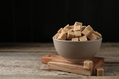 Photo of Bowl with brown sugar cubes on wooden table. Space for text