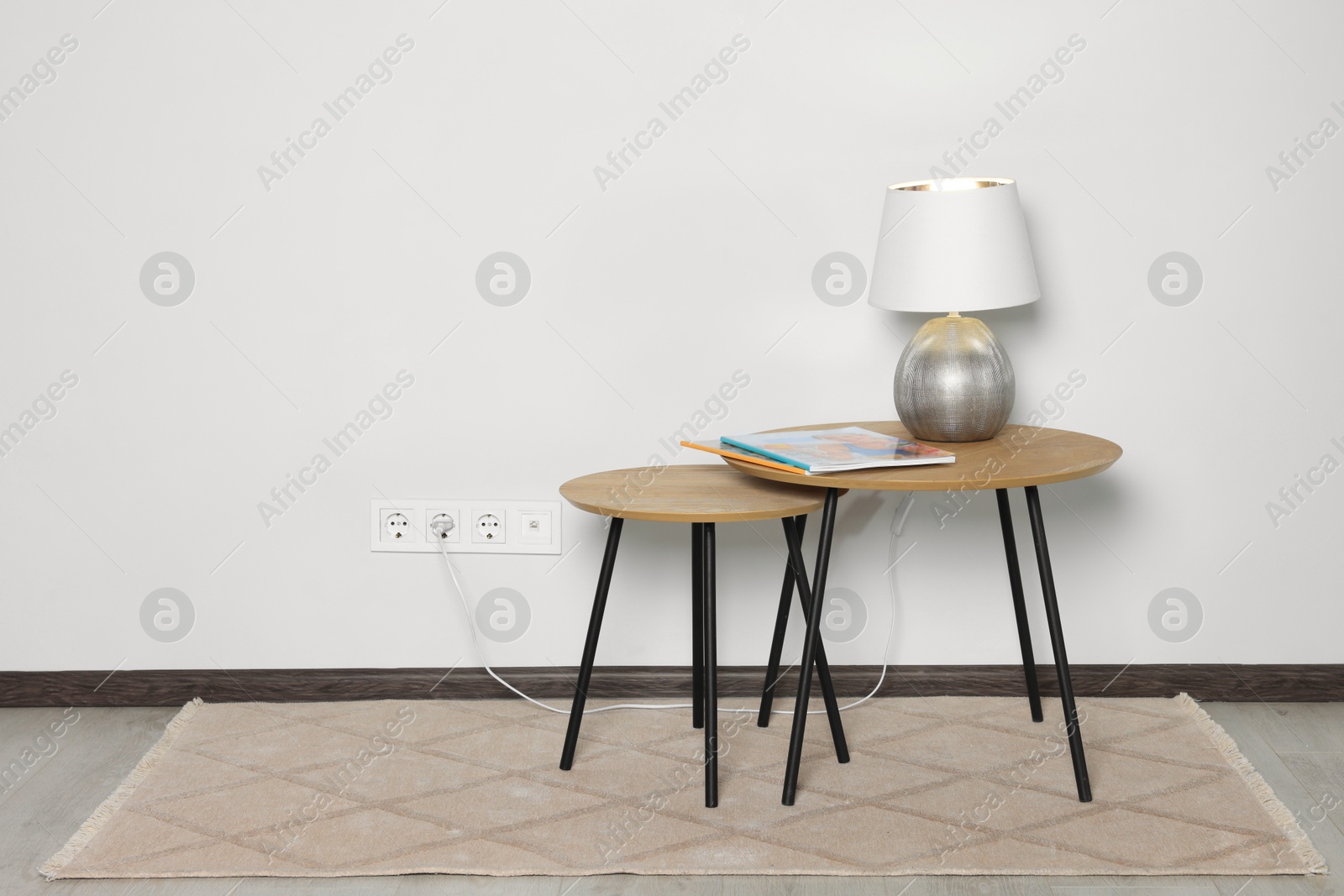 Photo of Lamp with magazines on wooden table near white wall, space for text