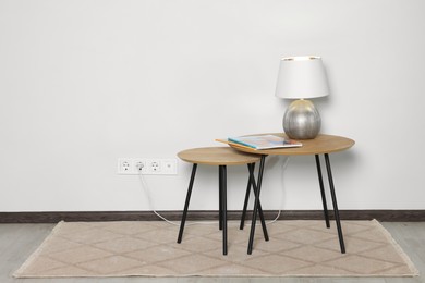 Lamp with magazines on wooden table near white wall, space for text