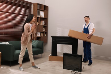 Photo of Young woman and professional technician with electric fireplace in room. Installing heater