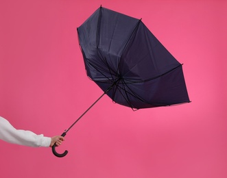 Photo of Woman with umbrella caught in gust of wind on pink background, closeup