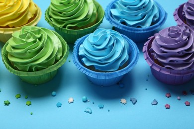 Many tasty cupcakes with bright cream and sprinkles on light blue background, above view