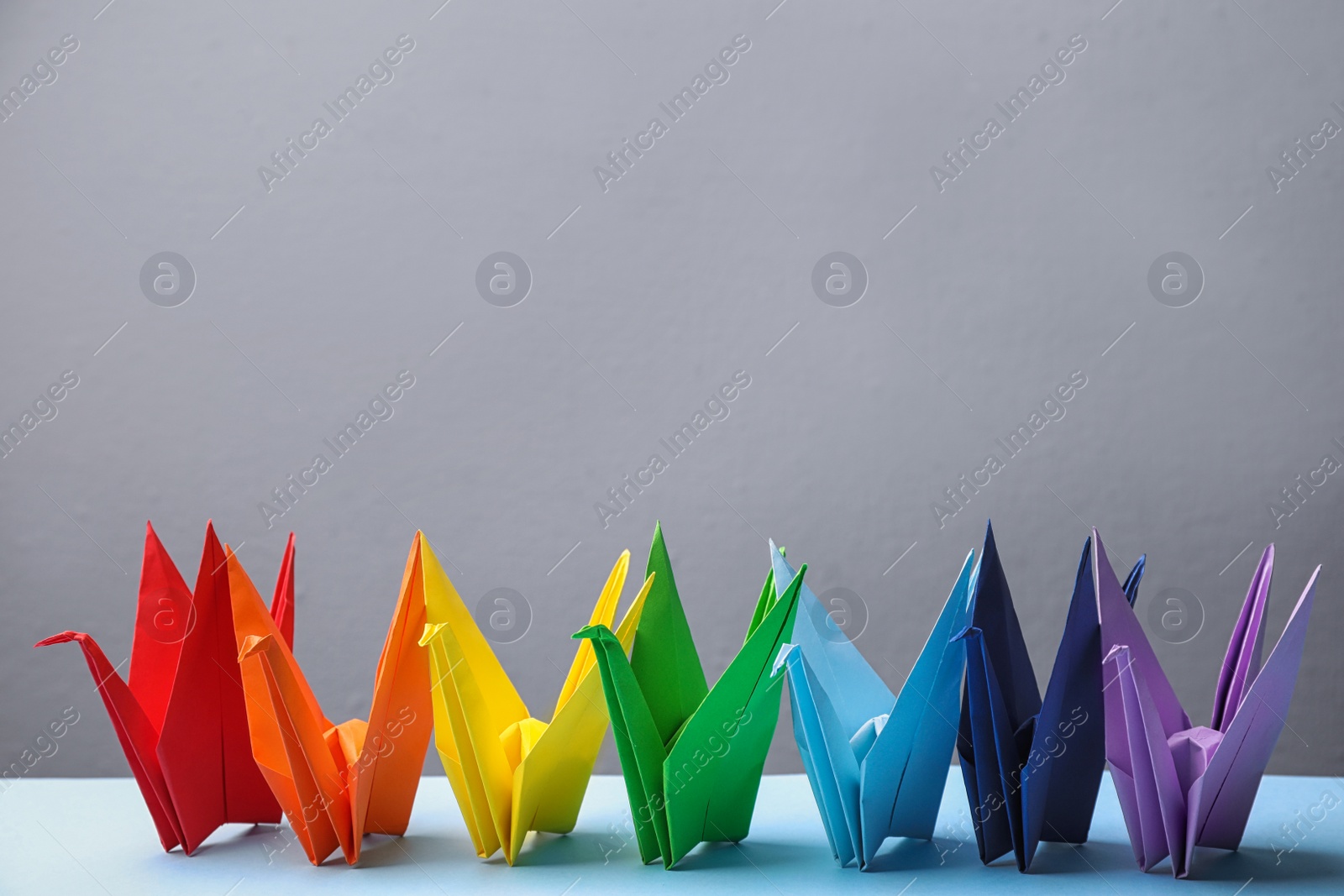 Photo of Colorful origami figures on light blue table. Rainbow palette