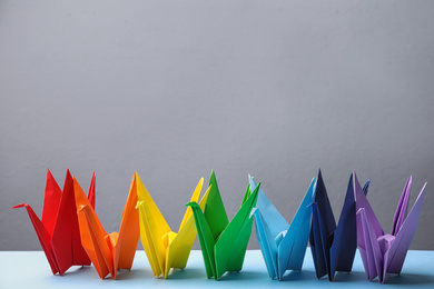 Colorful origami figures on light blue table. Rainbow palette