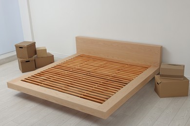 Photo of New wooden bed frame and moving boxes indoors