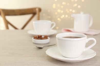 Cup of aromatic coffee on white wooden table indoors, space for text. Bokeh effect