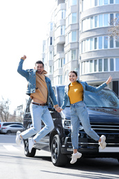 Happy couple jumping near car on city street. Buying new auto