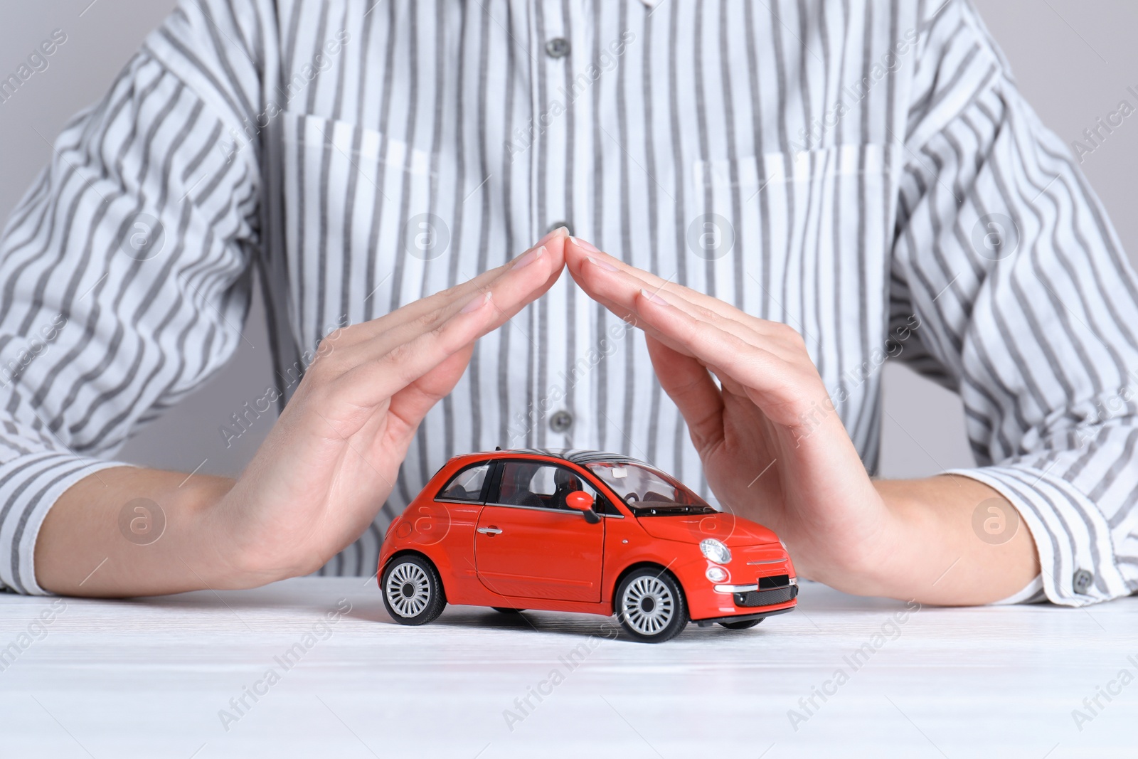 Photo of Insurance agent covering toy car on table, closeup