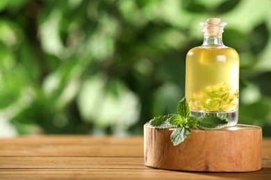Photo of Glass bottle of nettle oil and leaves on wooden table against blurred background, space for text