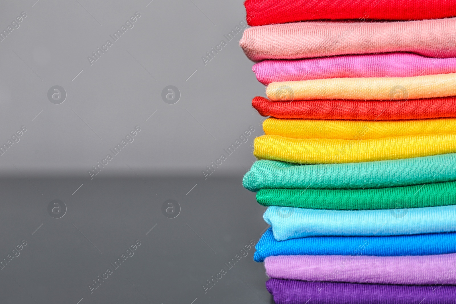 Photo of Stack of colorful t-shirts on table against gray background