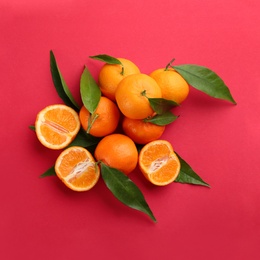 Fresh ripe tangerines with green leaves on red background, flat lay
