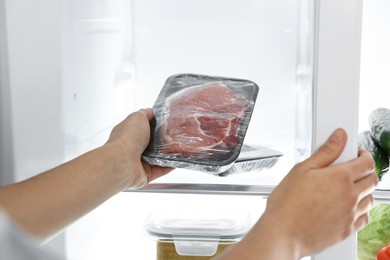 Photo of Young woman taking pack of meat out of refrigerator, closeup