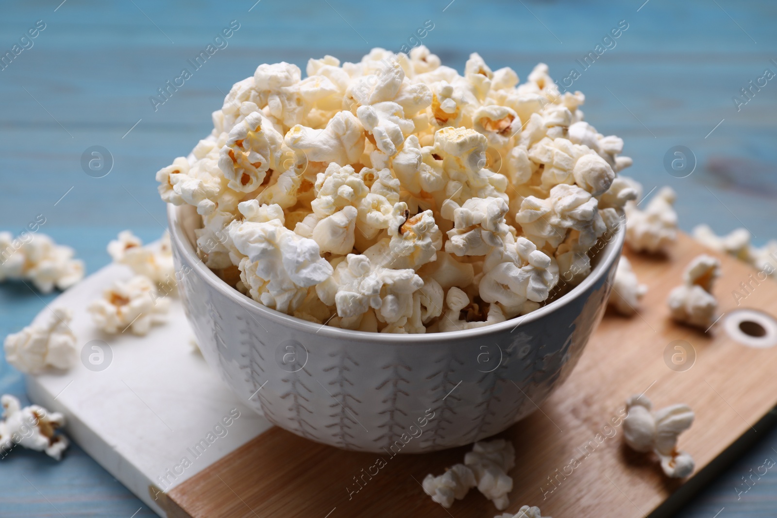 Photo of Tasty popcorn on light blue wooden table, closeup