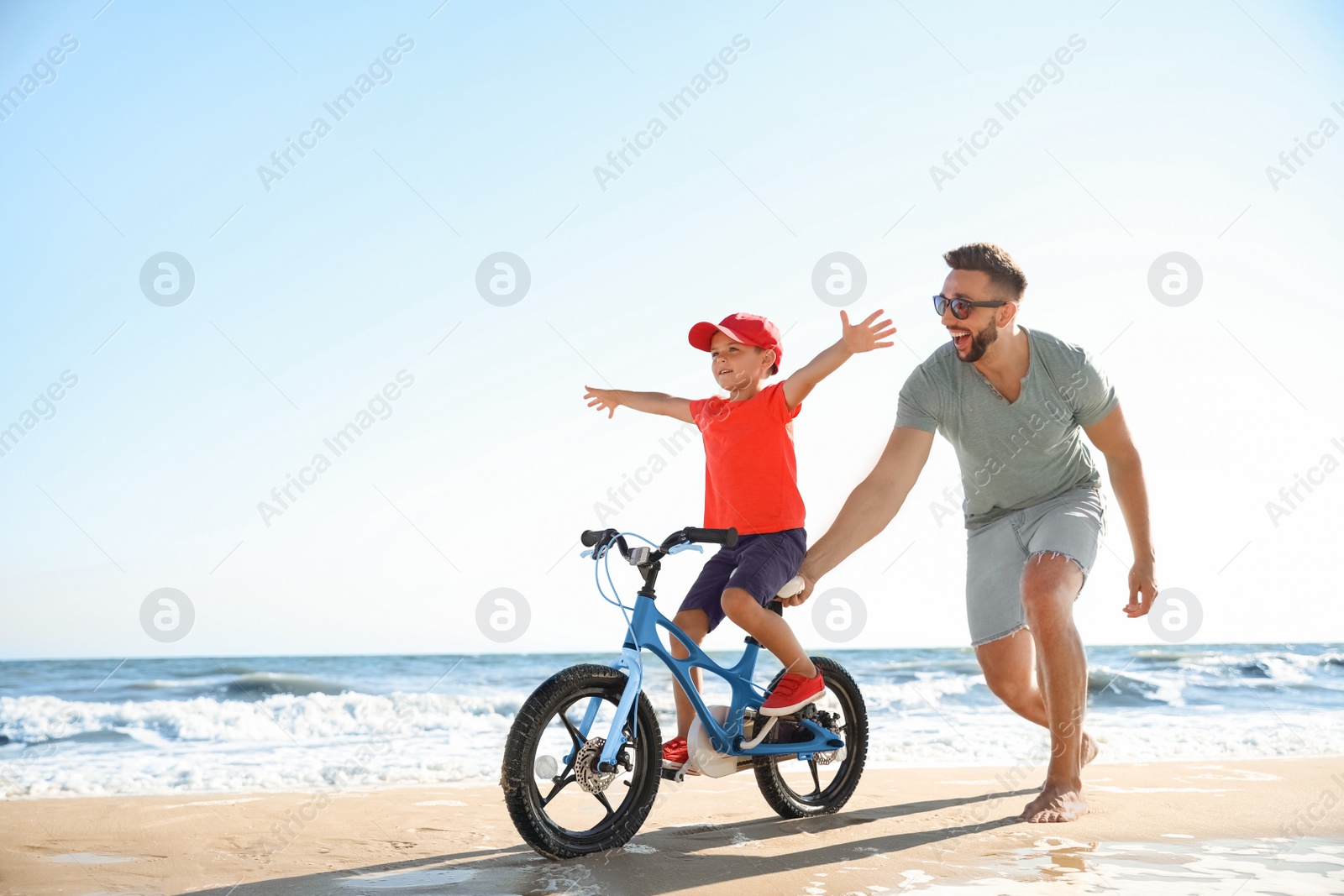 Photo of Happy father teaching son to ride bicycle on sandy beach near sea