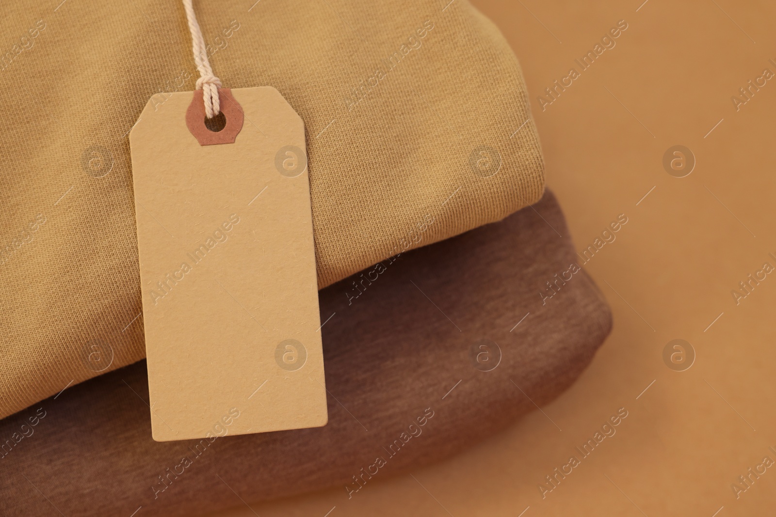 Photo of Garment with cardboard tag on beige background, closeup. Space for text