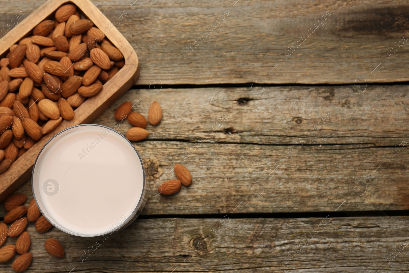 Photo of Glass of almond milk and almonds on wooden table, top view. Space for text
