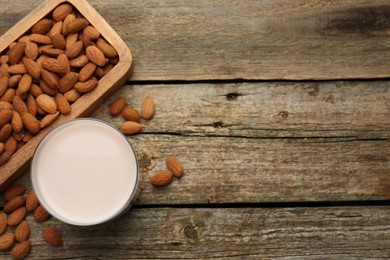 Glass of almond milk and almonds on wooden table, top view. Space for text