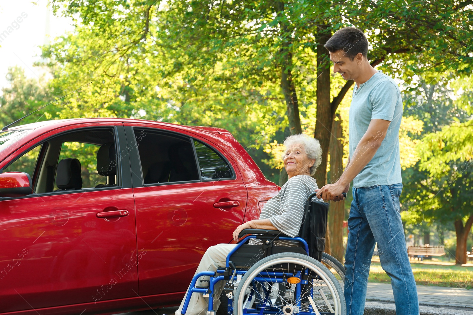 Photo of Young man with disabled senior woman in wheelchair near car outdoors