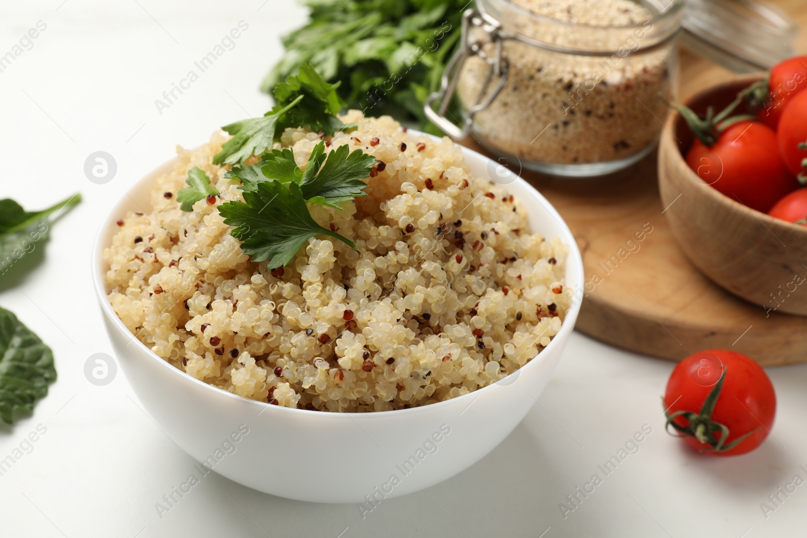 Photo of Tasty quinoa porridge with parsley in bowl on white table, closeup