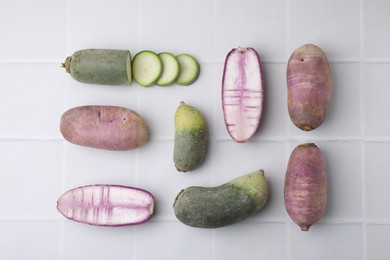Photo of Purple and green daikon radishes on white tiled table, flat lay