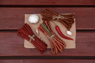 Photo of Bundles of delicious kabanosy with rosemary, peppercorn, garlic and chilli on wooden table, top view