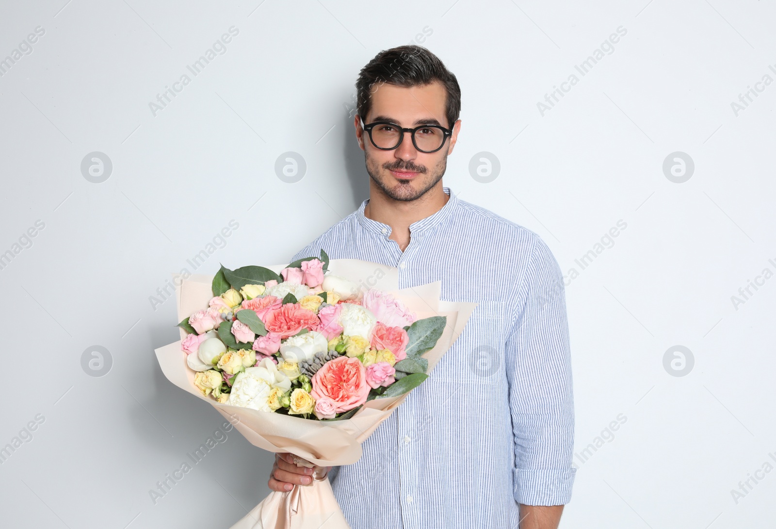 Photo of Young handsome man with beautiful flower bouquet on light background