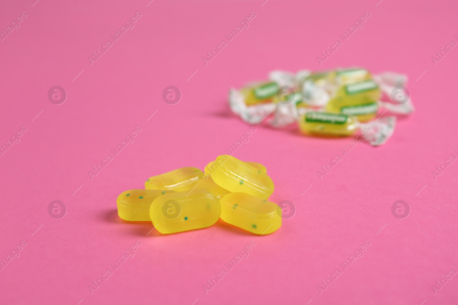 Photo of Pile of tasty lemon drops on pink background