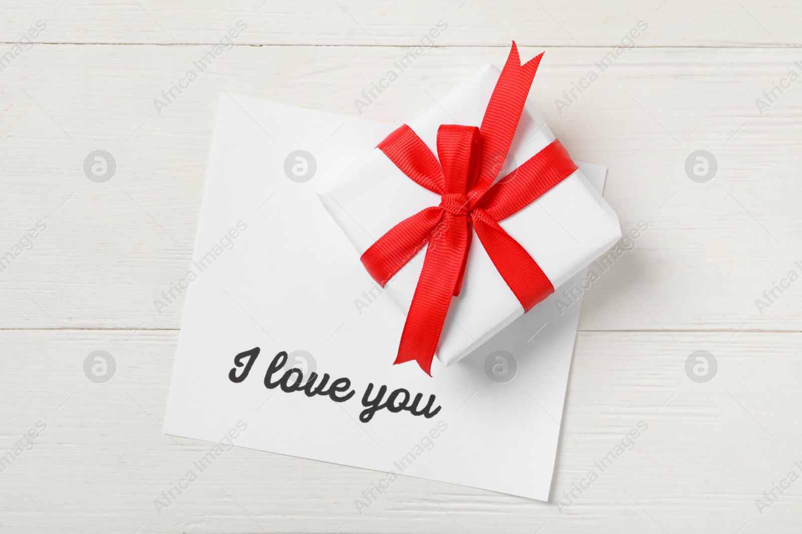 Photo of Card with text I Love You and gift box on white wooden table, top view