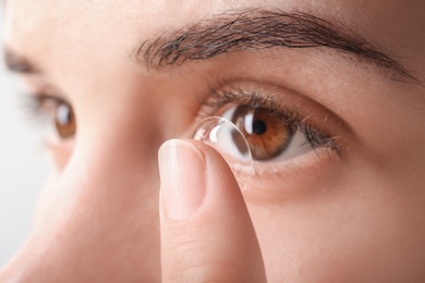 Photo of Young woman putting contact lens in her eye, closeup