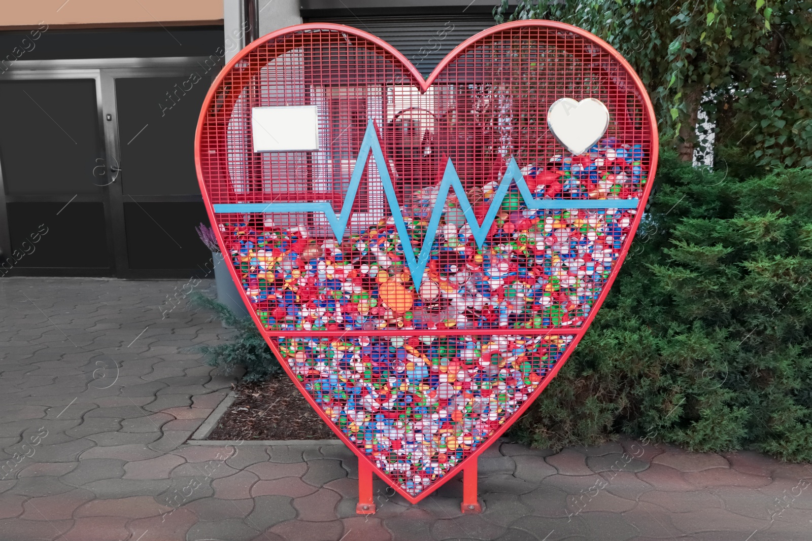 Photo of Heart shaped red recycling container for plastic caps outdoors