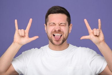 Happy man showing his tongue and rock gesture on purple background