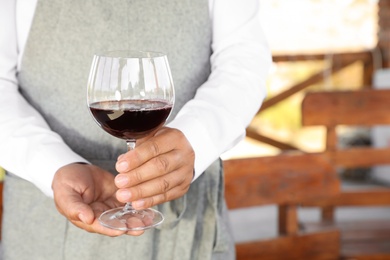 Photo of Waiter holding glass of red wine in outdoor cafe, closeup. Space for text