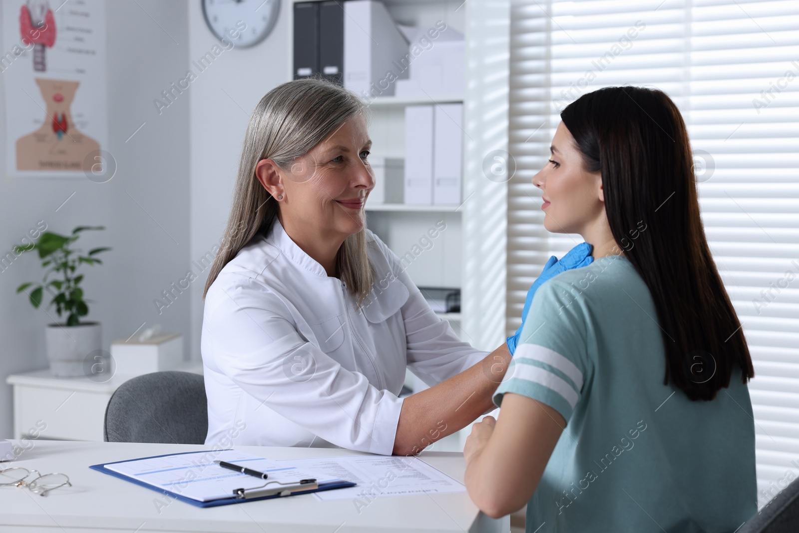 Photo of Endocrinologist examining thyroid gland of patient at table in hospital