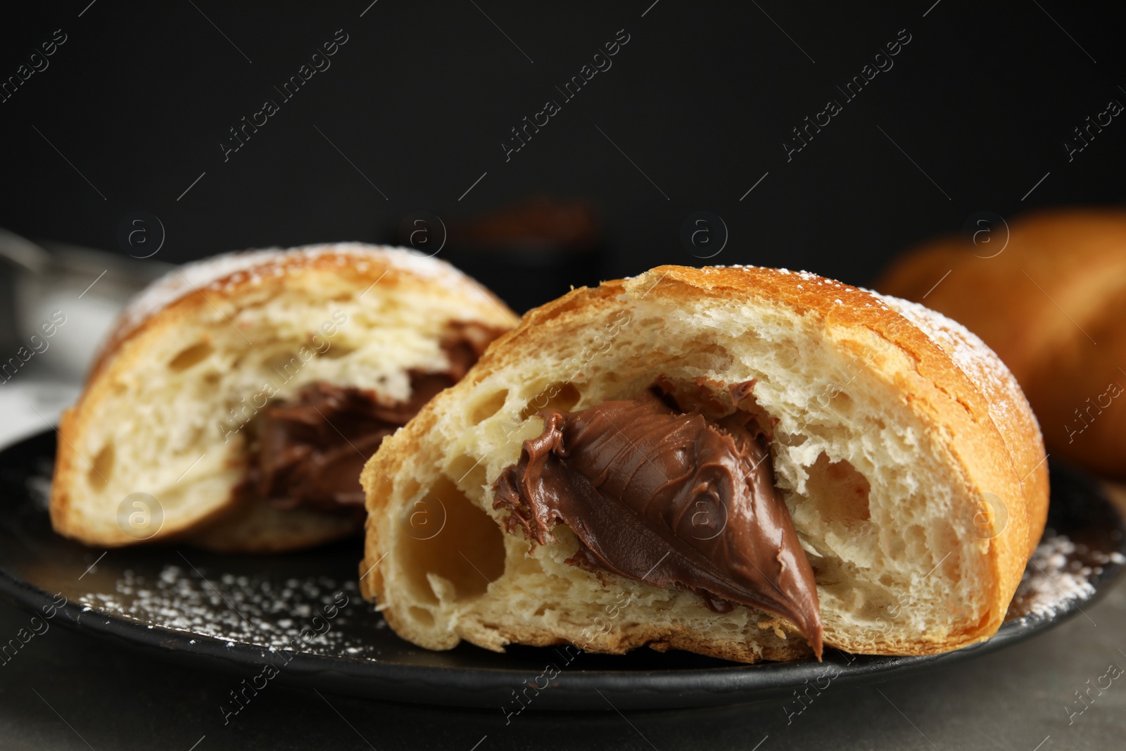Photo of Tasty croissant with chocolate and sugar powder on black plate, closeup