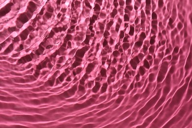 Rippled surface of clear water on bright pink background, top view