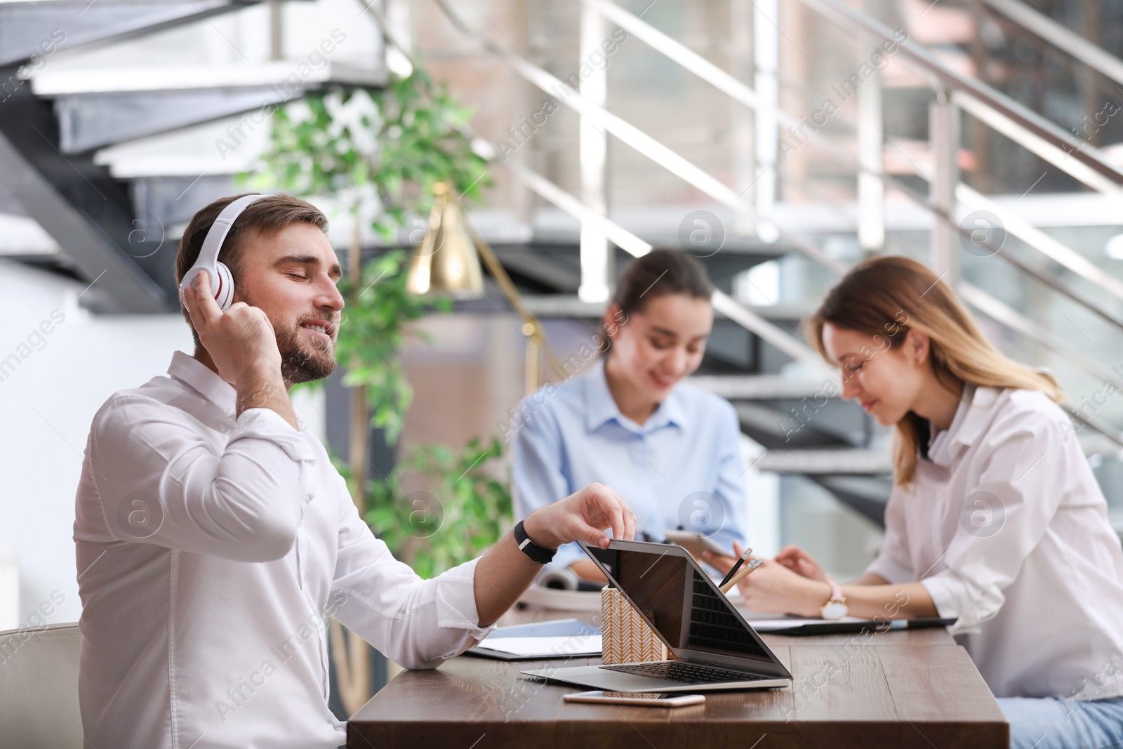 Photo of Young businessman with headphones, laptop and his colleagues at table in office