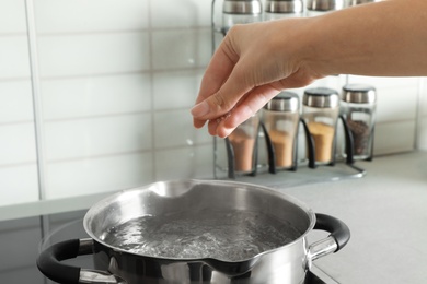 Photo of Woman salting boiling water in pot on stove, closeup
