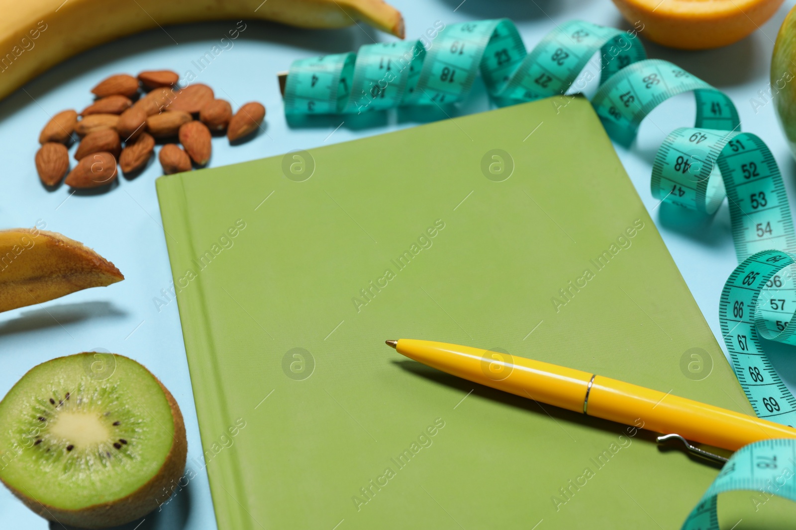 Photo of Weight loss concept. Composition with notebook, measuring tape and different products on light blue background, closeup