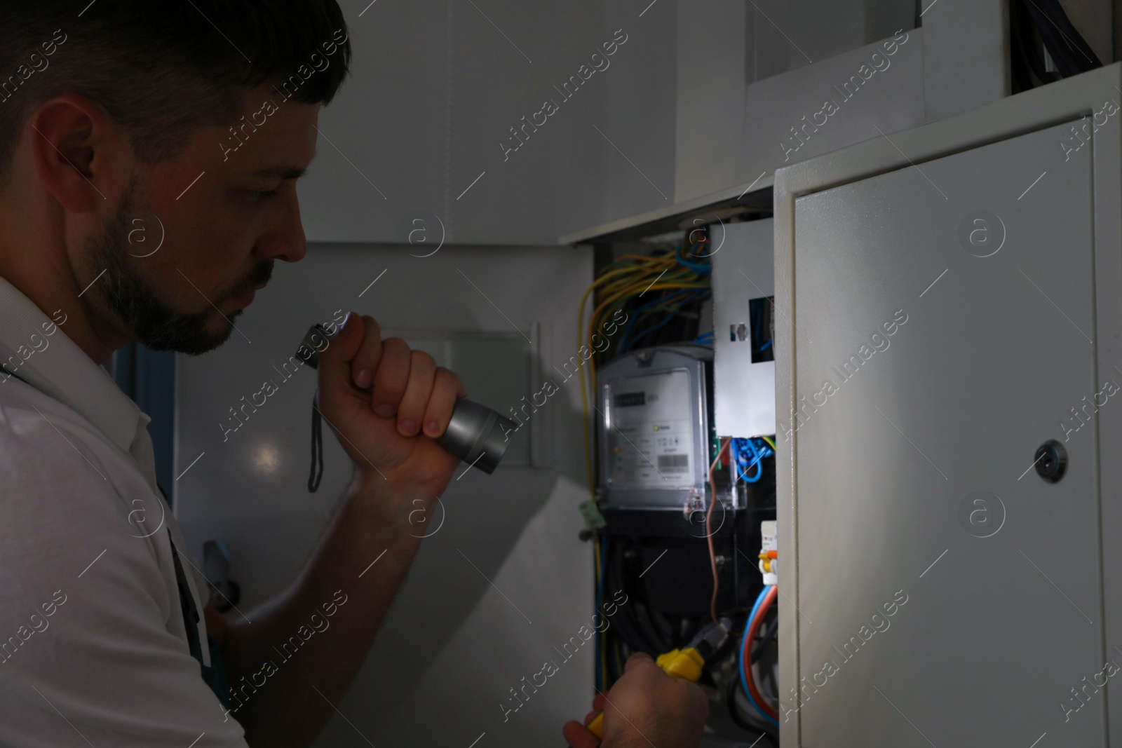 Photo of Electrician with flashlight fixing electric panel indoors