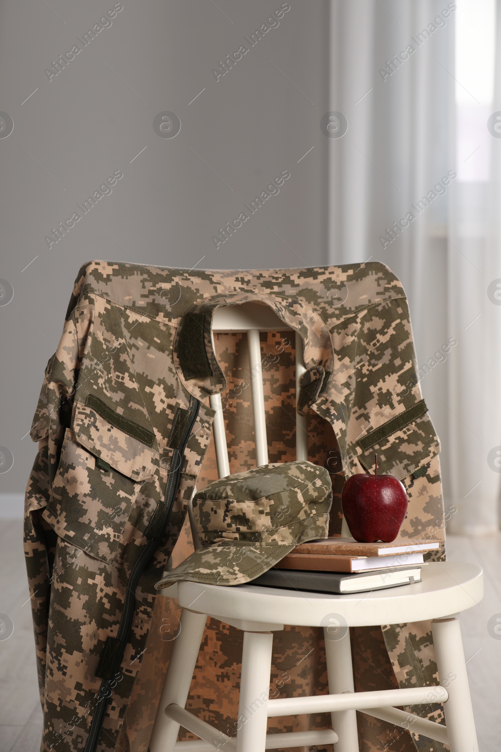 Photo of Chair with soldier uniform, notebooks and apple indoors. Military education