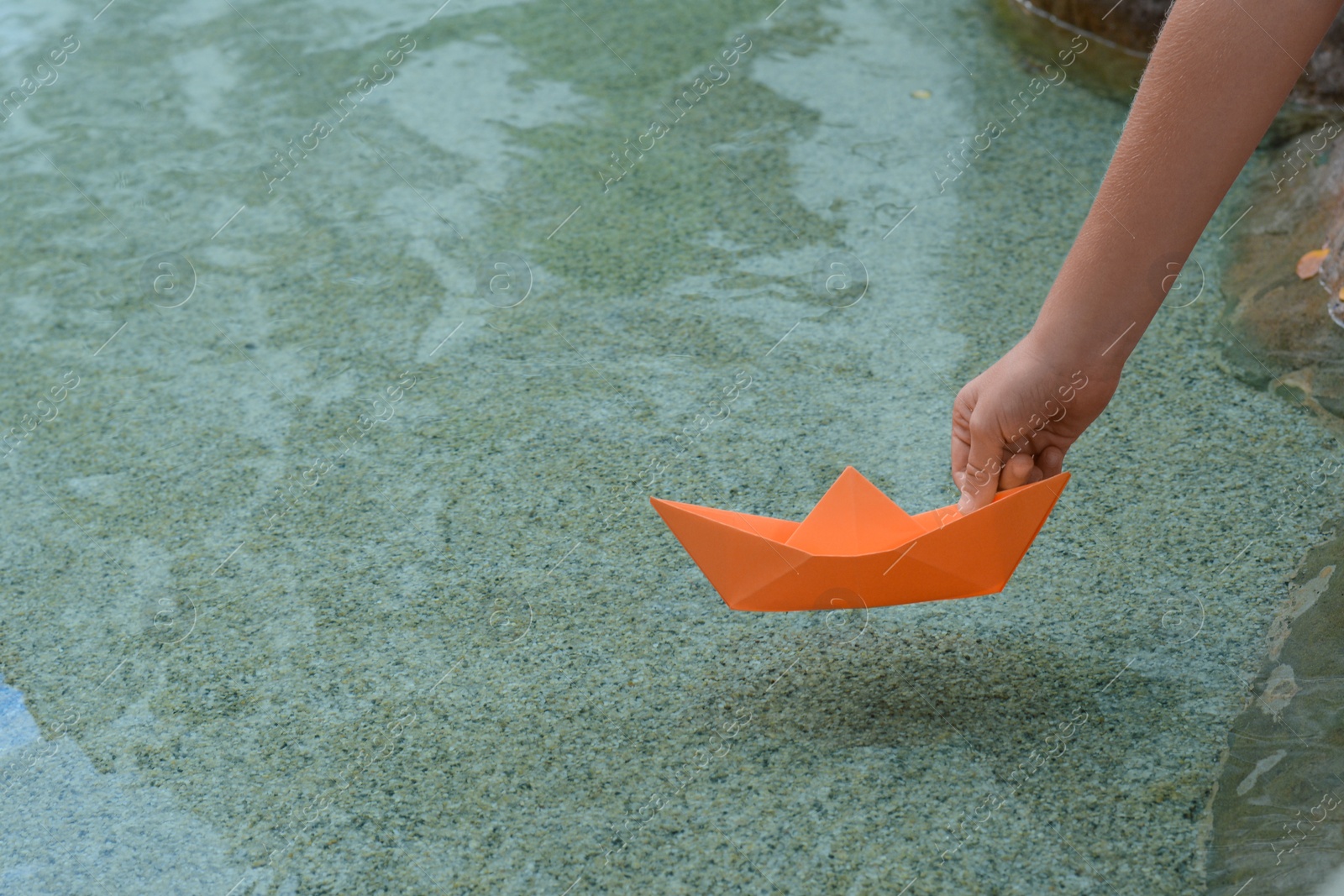 Photo of Kid launching small orange paper boat on water outdoors, closeup. Space for text