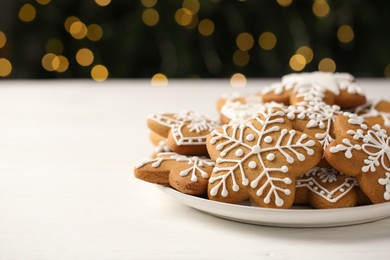 Photo of Tasty Christmas cookies with icing on white wooden table against blurred lights, closeup. Space for text