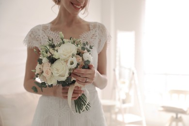 Young bride with beautiful wedding bouquet in room, closeup. Space for text