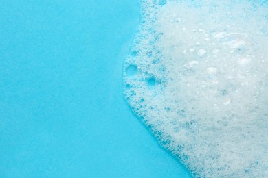 Photo of Fluffy bath foam on turquoise background, top view. Space for text