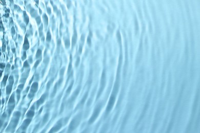 Rippled surface of clear water on light blue background, closeup