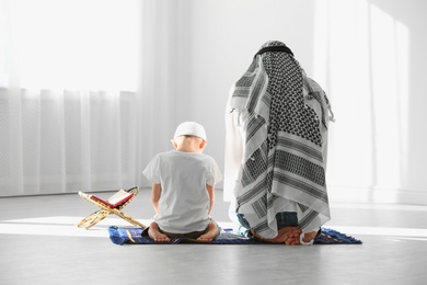 Photo of Muslim man and his son praying together indoors