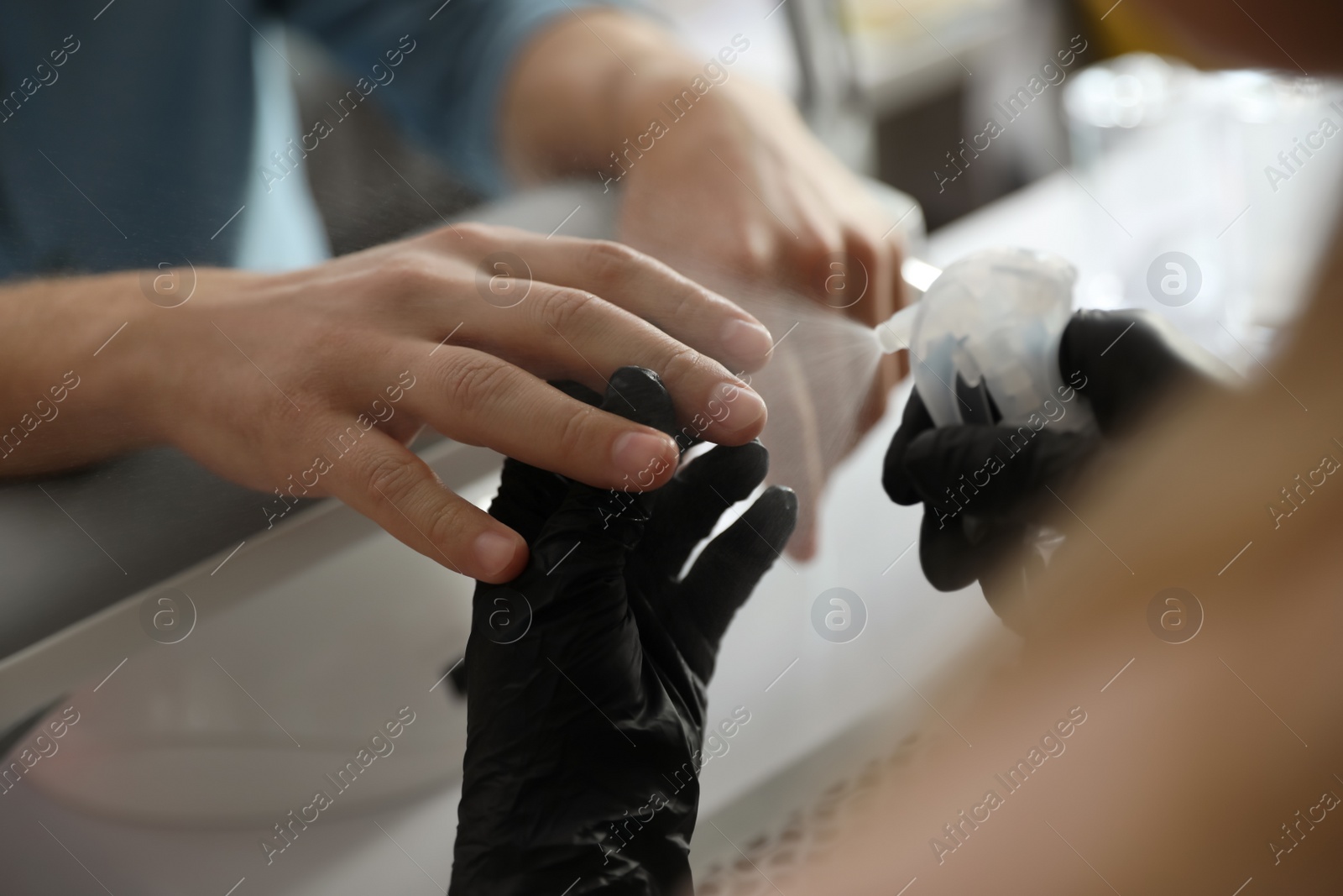 Photo of Professional manicurist applying antiseptic on client's hands in beauty salon, closeup