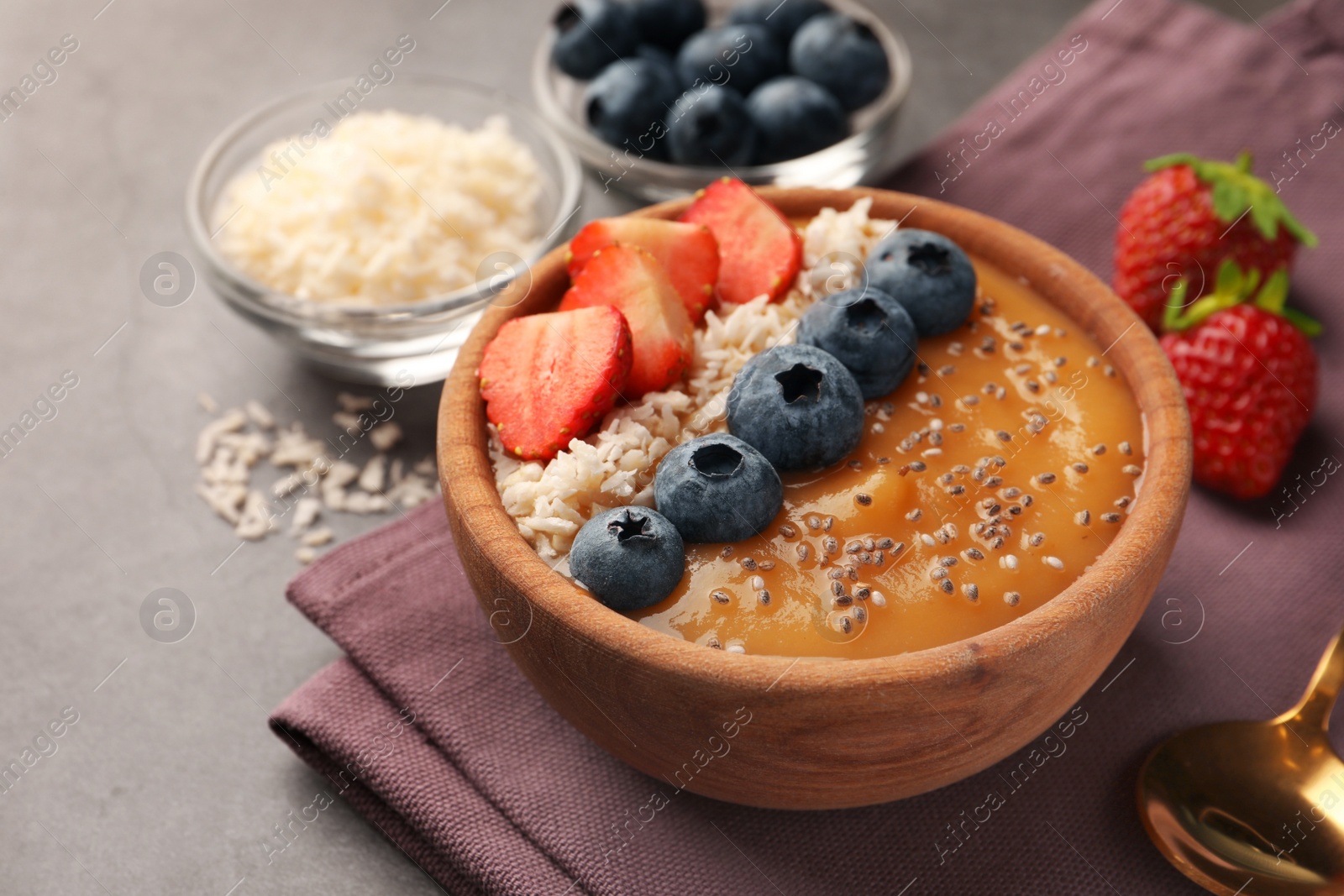 Photo of Delicious smoothie bowl with fresh berries, chia seeds and coconut flakes on grey table, closeup