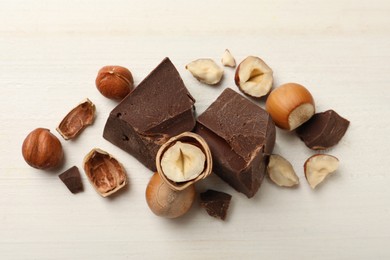 Delicious chocolate chunks and hazelnuts on white table, flat lay